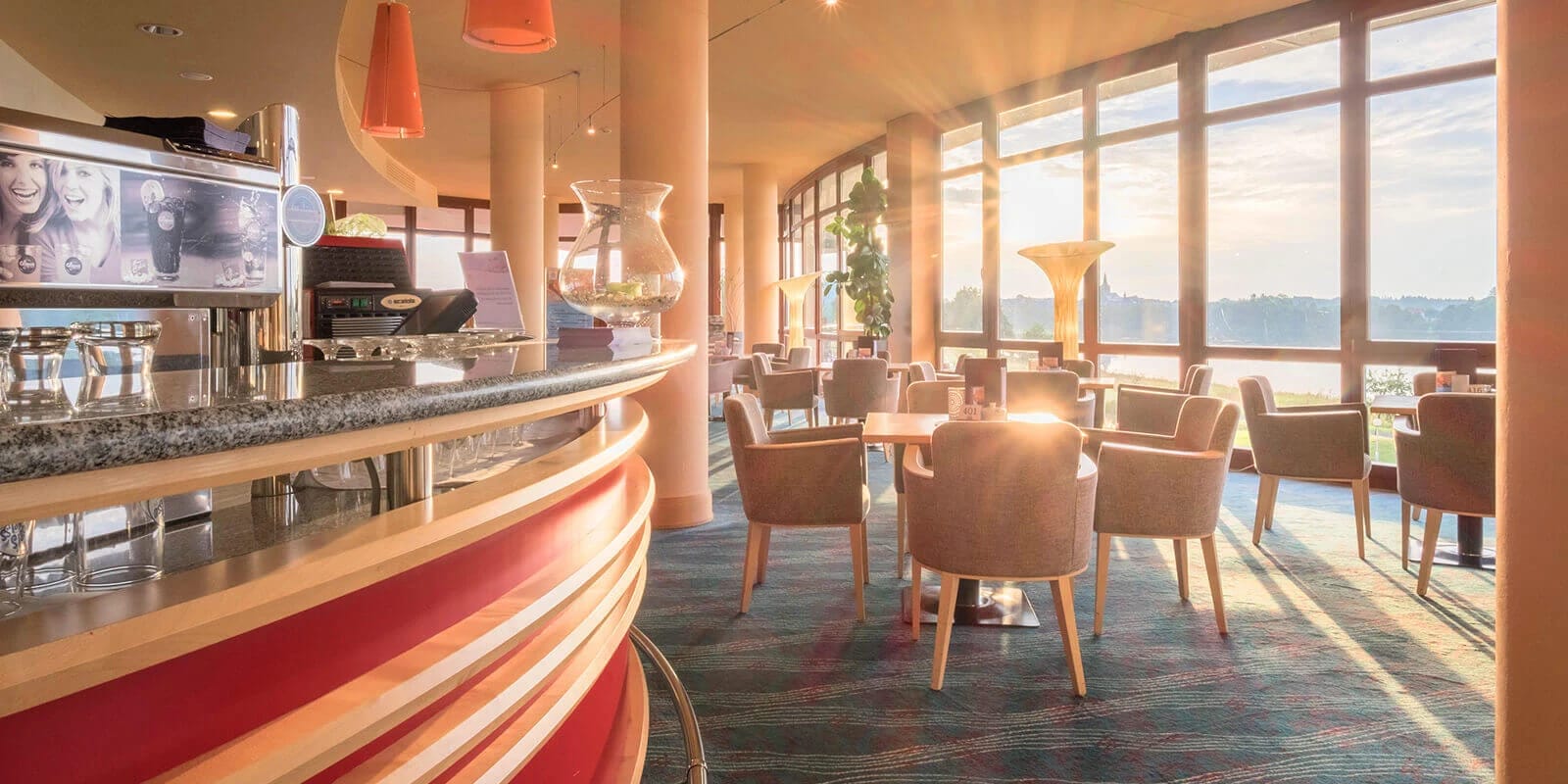Lobby-Bar mit Sesseln, runder Theke und Panoramafenstern im Abendlicht