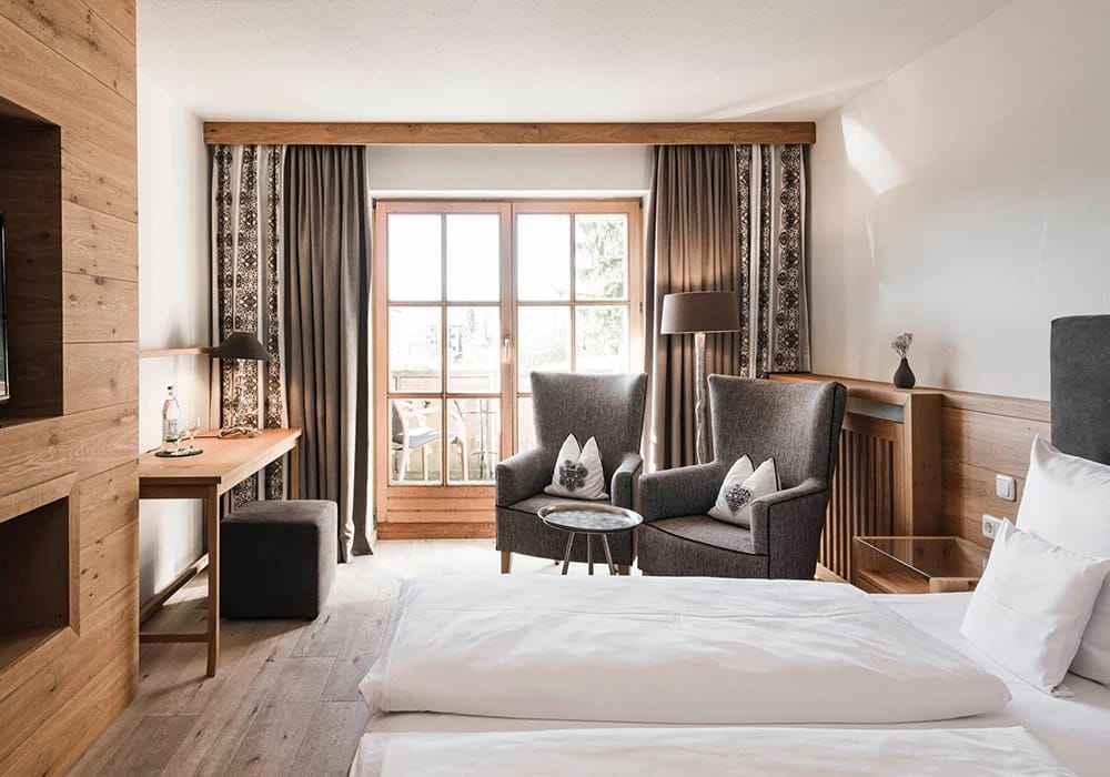Zimmer mit Doppelbett, Holzwand und zwei Sesseln vor der Balkontür