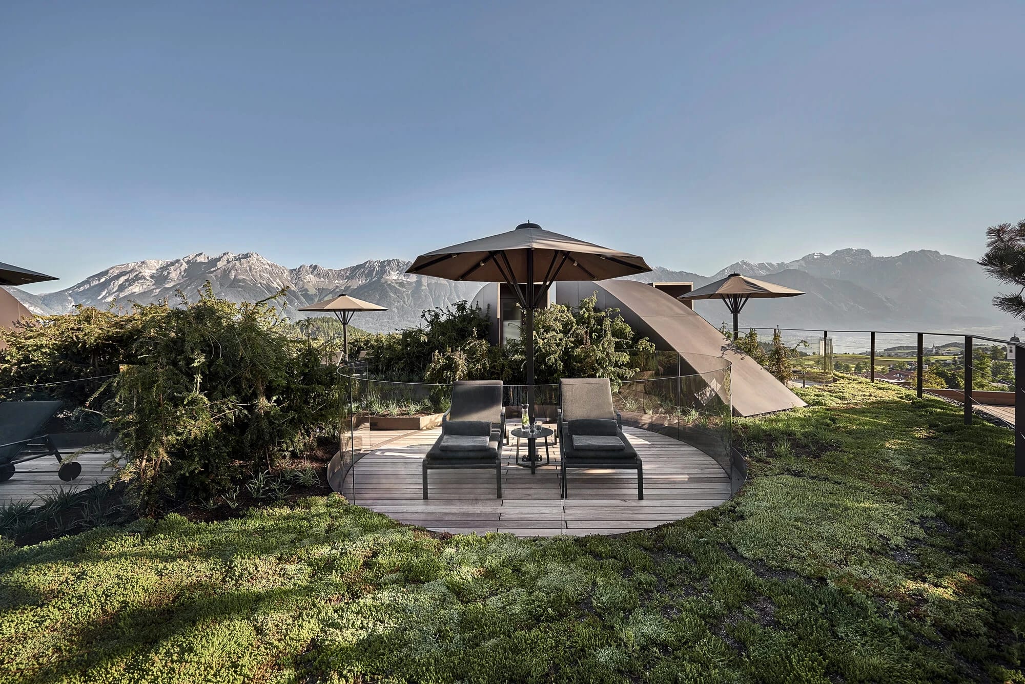 Dachterrasse mit Liegen und Sonnenschirmen auf begrüntem Dach, Blick auf die Berge