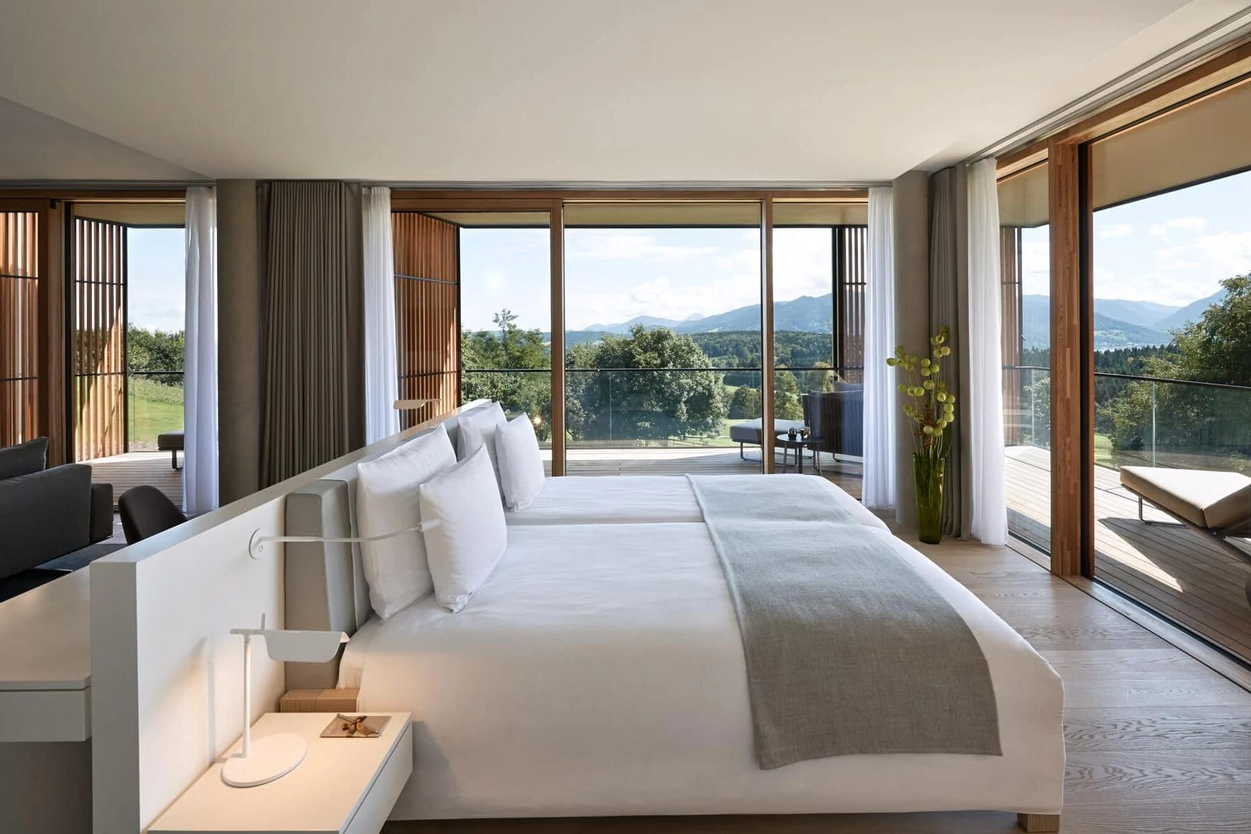 Schlafzimmer einer Suite mit bodentiefen Fenstern, Terrasse und Blick über Wiesen zu den Bergen
