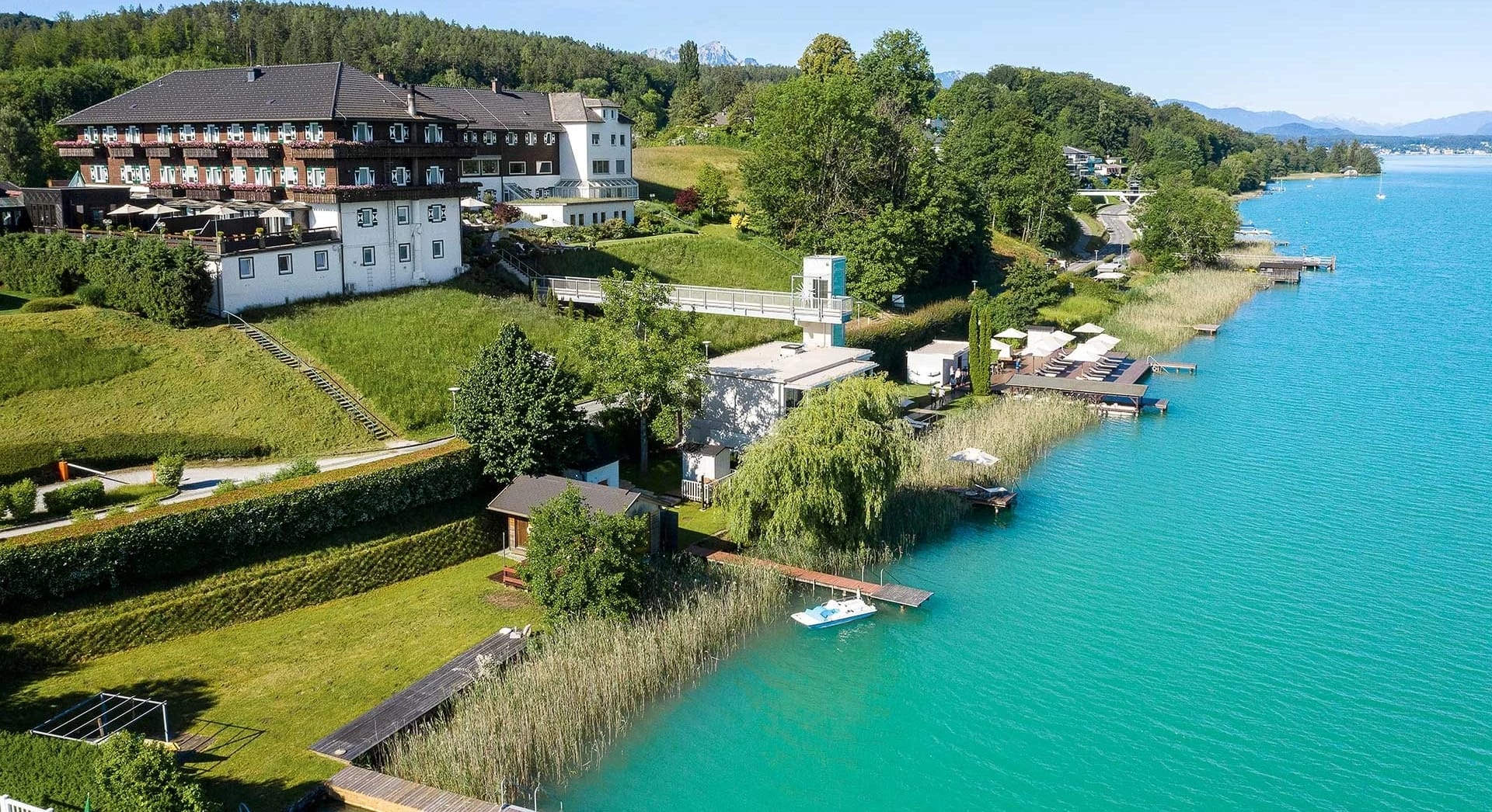 Hotelgebäude mit Garten und Liegeterrasse direkt am türkisfarbenen Wörthersee