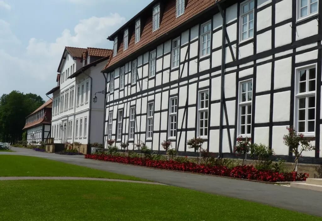 Weiß-schwarze Fachwerkfassade eines Logierhauses mit rotem Blumenbeet und Rasenfläche davor