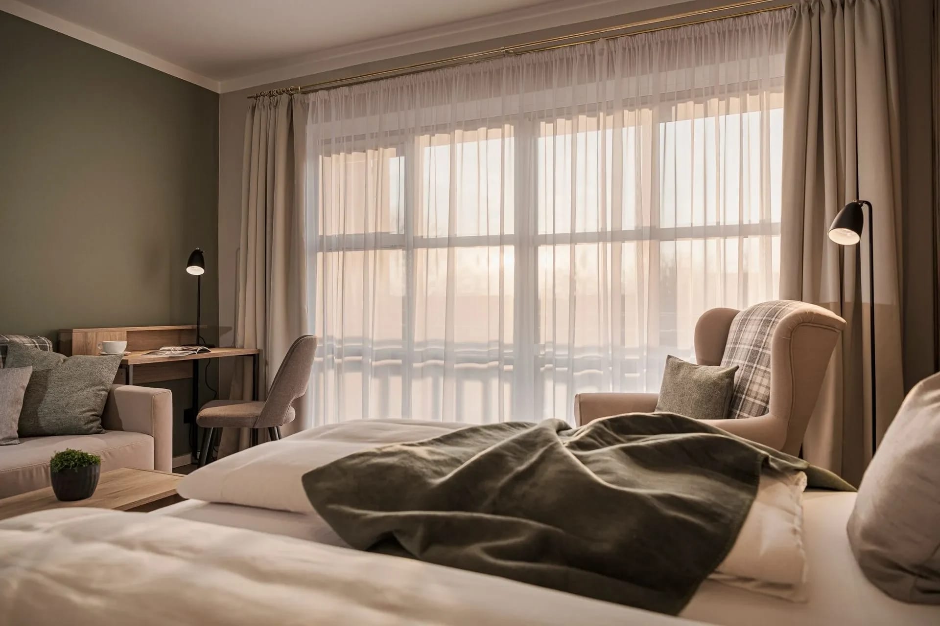 Doppelzimmer mit olivgrüner Wand, Schreibtisch, Sesseln und bodentiefem Fenster