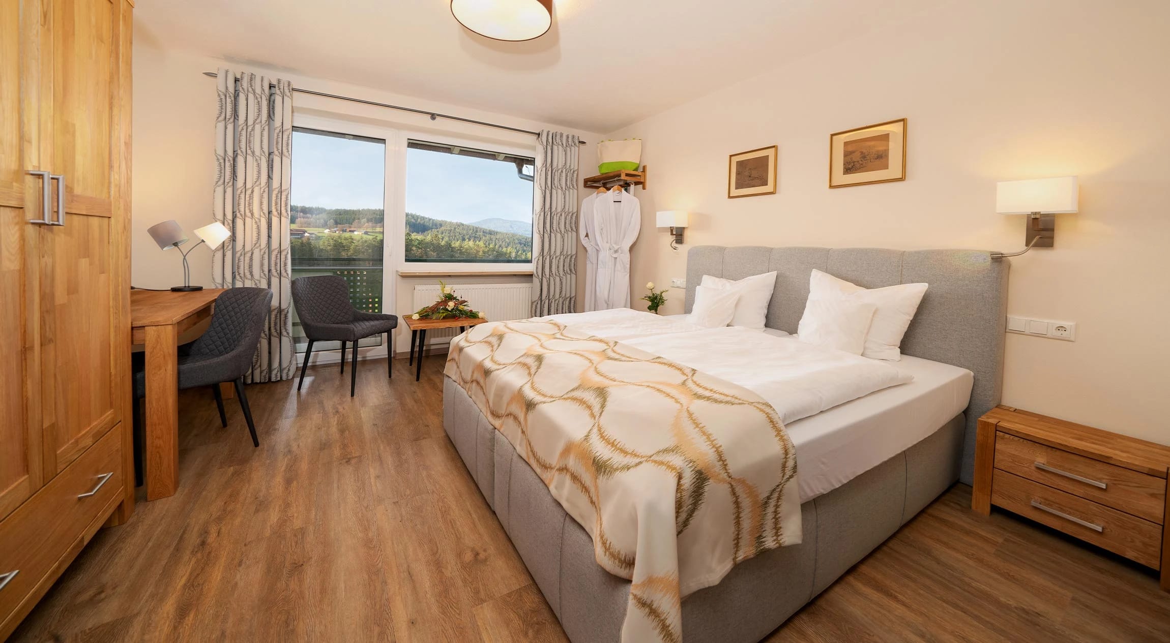 Doppelzimmer mit Boxspringbett, Schreibtisch mit Sesseln und Fenster mit Blick ins Grüne