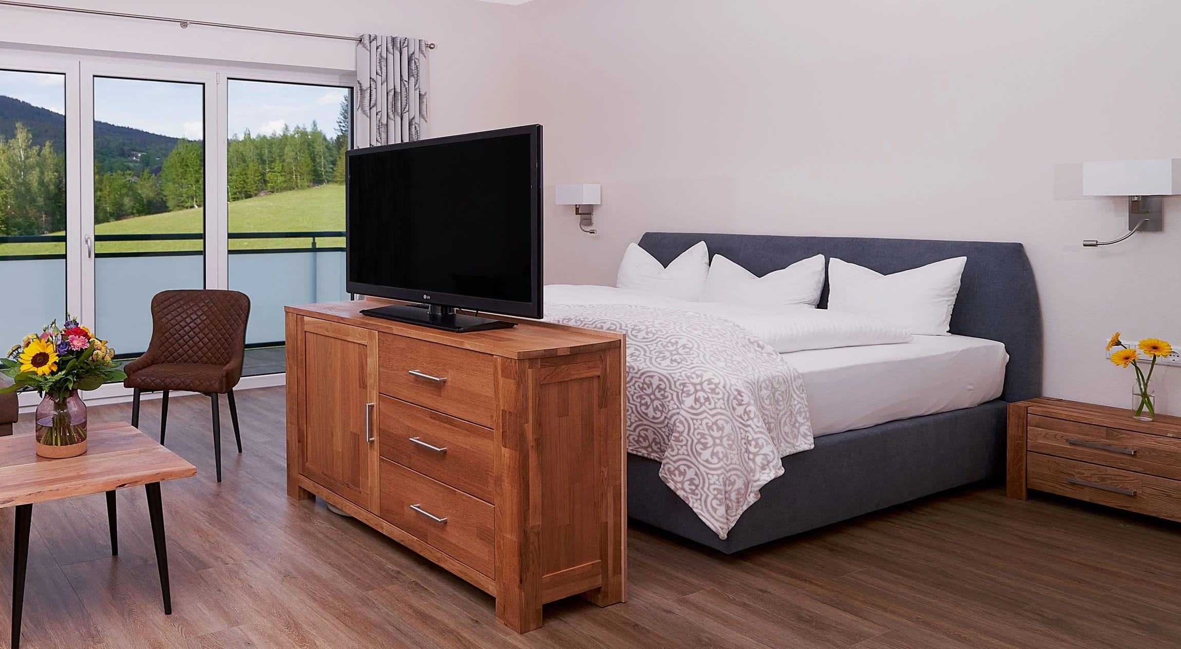 Studio mit Doppelbett, Fernseher auf Holzkommode und Sitzbereich am Fenster mit Landschaftsblick