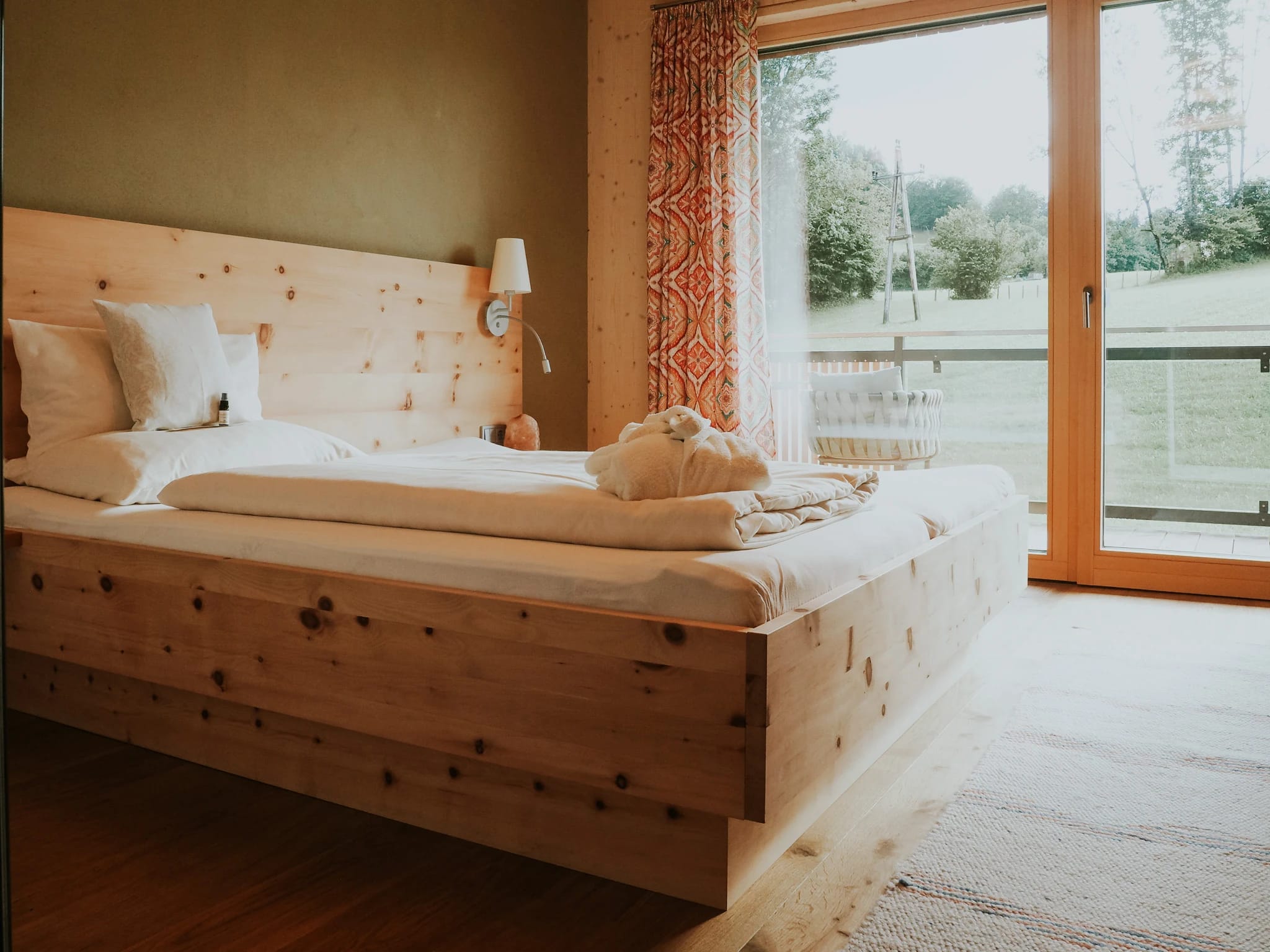Schlafzimmer mit Zirbenbett und Blick durch die Balkontür ins Grüne