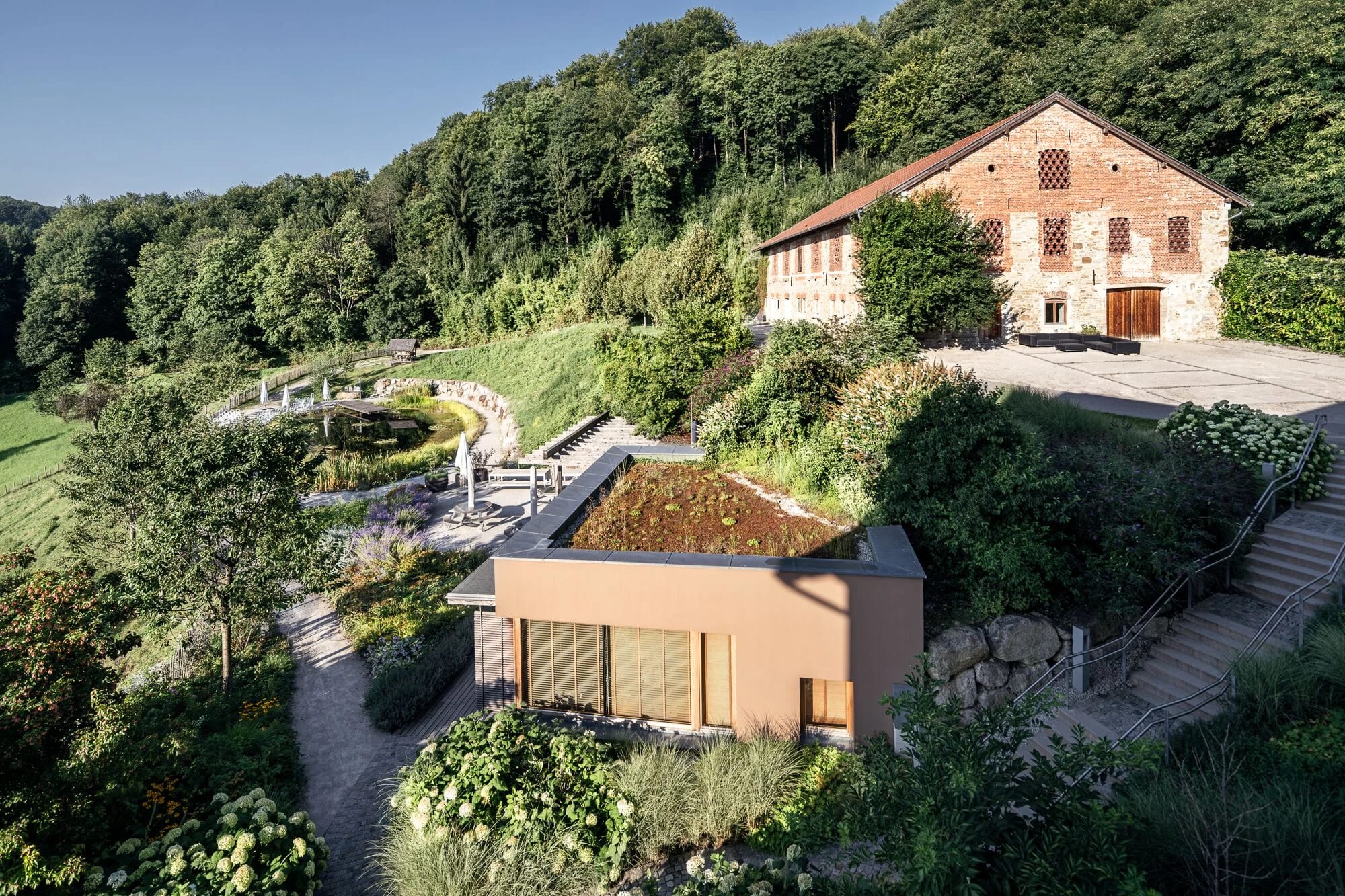 Flachdachbau mit begrüntem Dach und altes Backsteingebäude in der Gartenanlage am Waldrand