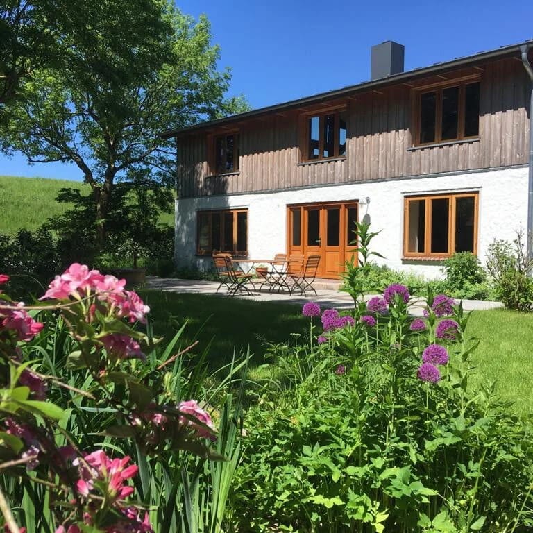 Haus am Seedeich mit Holzfassade, Sitzplatz vor der Tür und blühenden Stauden im Vorgarten