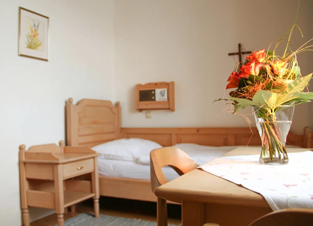 Zimmer mit Holzbett, Nachtkästchen und Tisch mit Blumenstrauß
