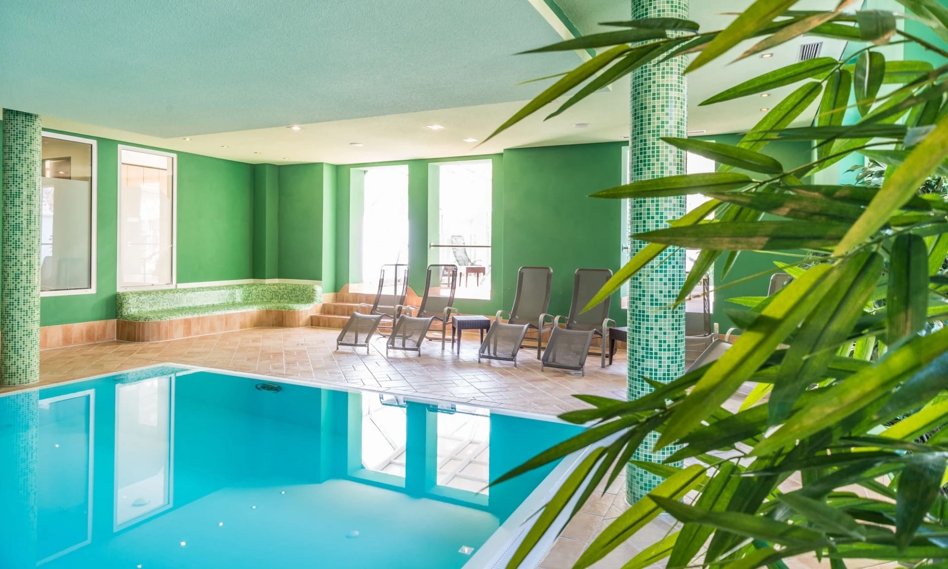 Innenpool mit türkisem Wasser und Liegen an der grünen Wand