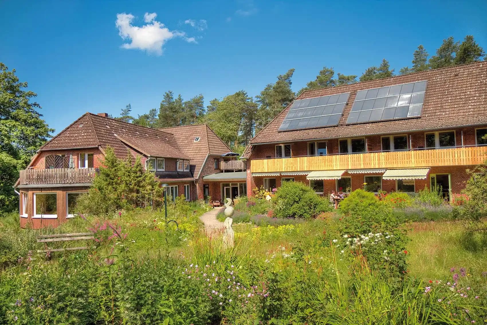 Hauptgebäude des Biohotel Spöktal mit Balkonen und Solardach hinter einem blühenden Naturgarten
