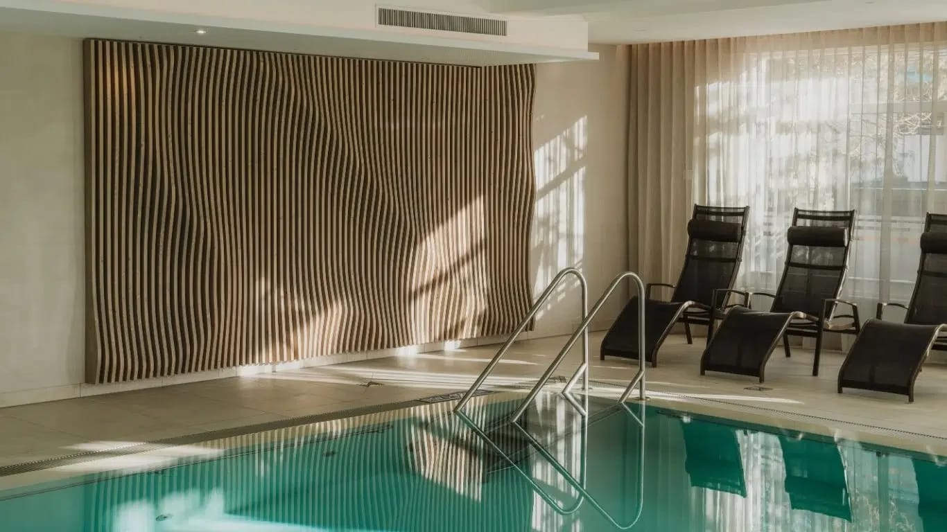 Innenpool im Spa mit geschwungener Holzwand und Ruheliegen