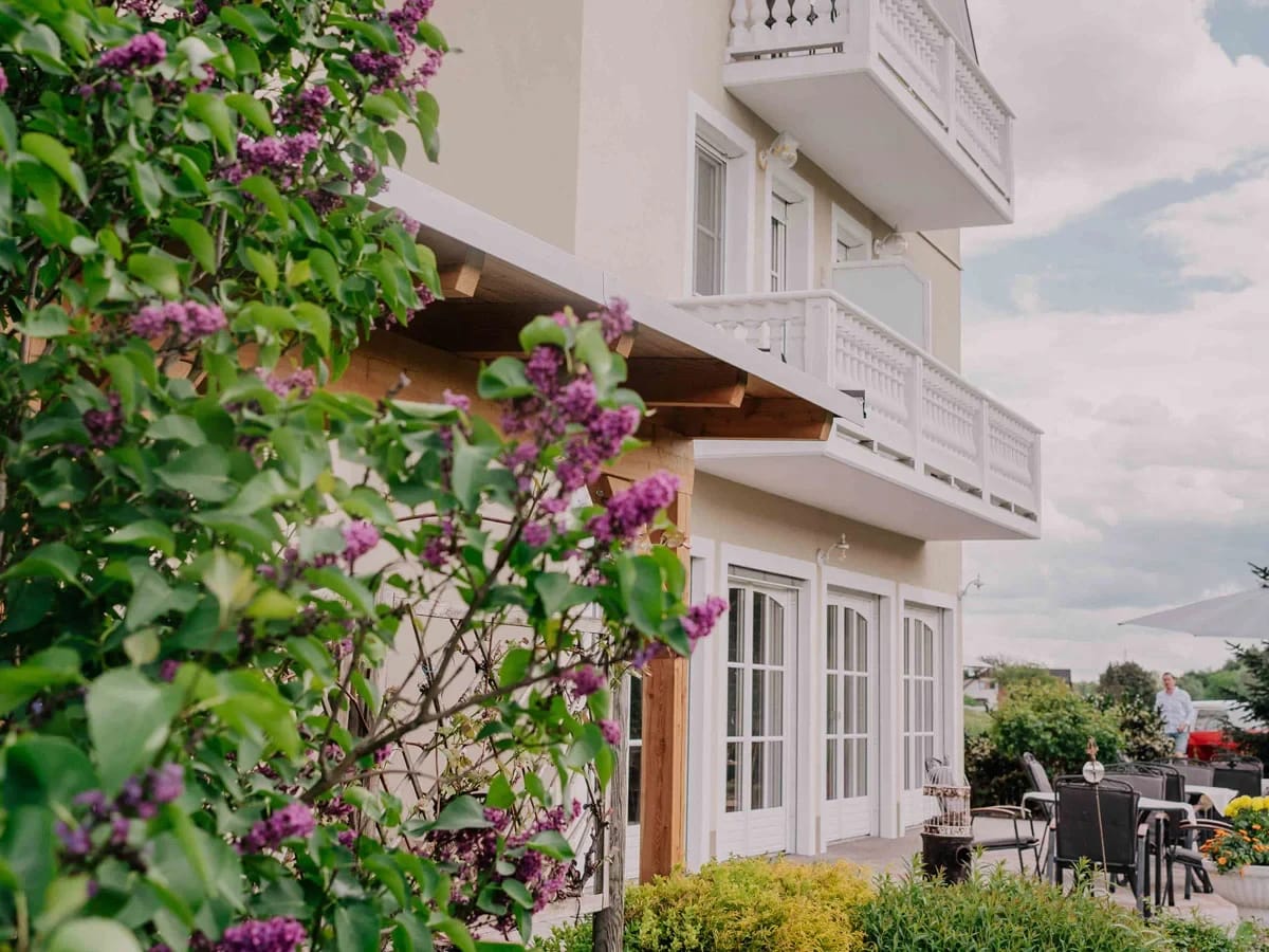 Hausfassade mit Balkonen und Terrassentüren hinter blühendem Flieder