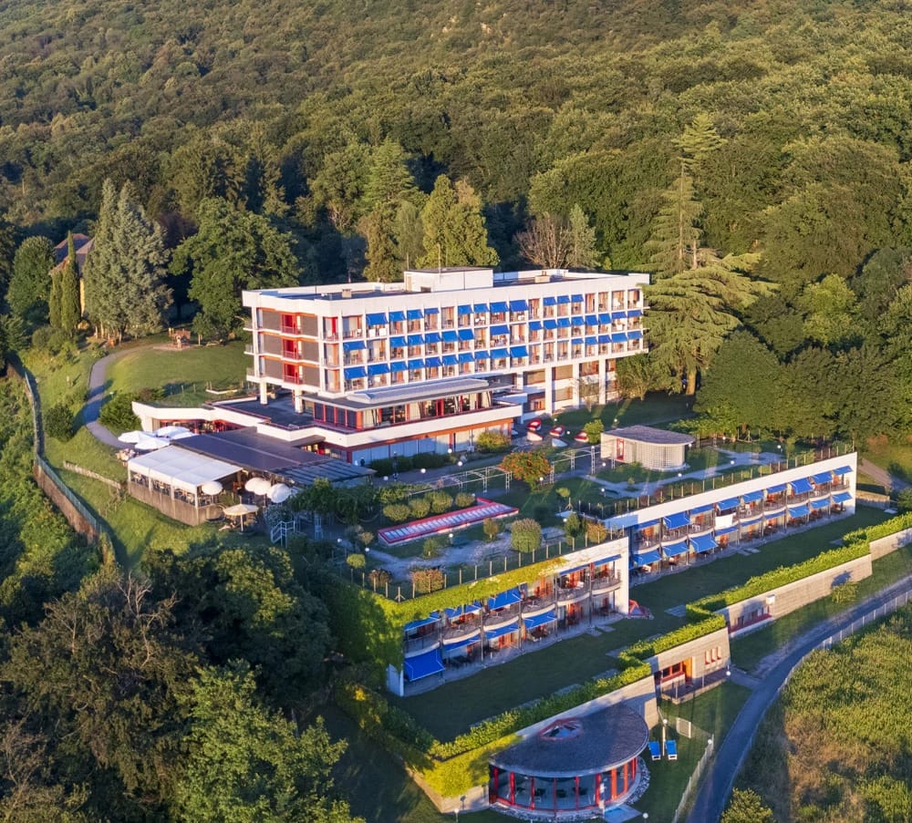 Luftaufnahme des Hotelgebäudes mit Balkonreihen, umgeben von bewaldeten Hängen
