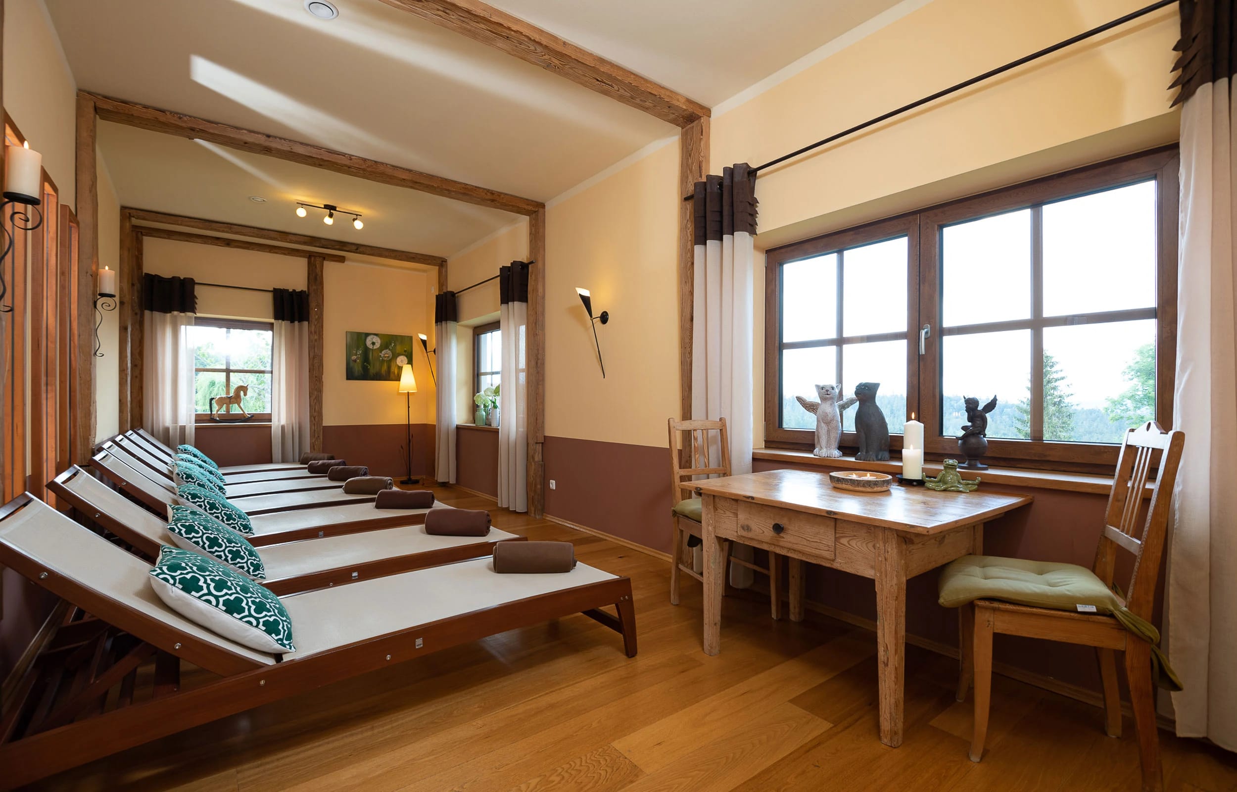 Ruheraum mit hölzernen Liegen, Holzbalken an der Decke und Fenstern mit Blick ins Grüne