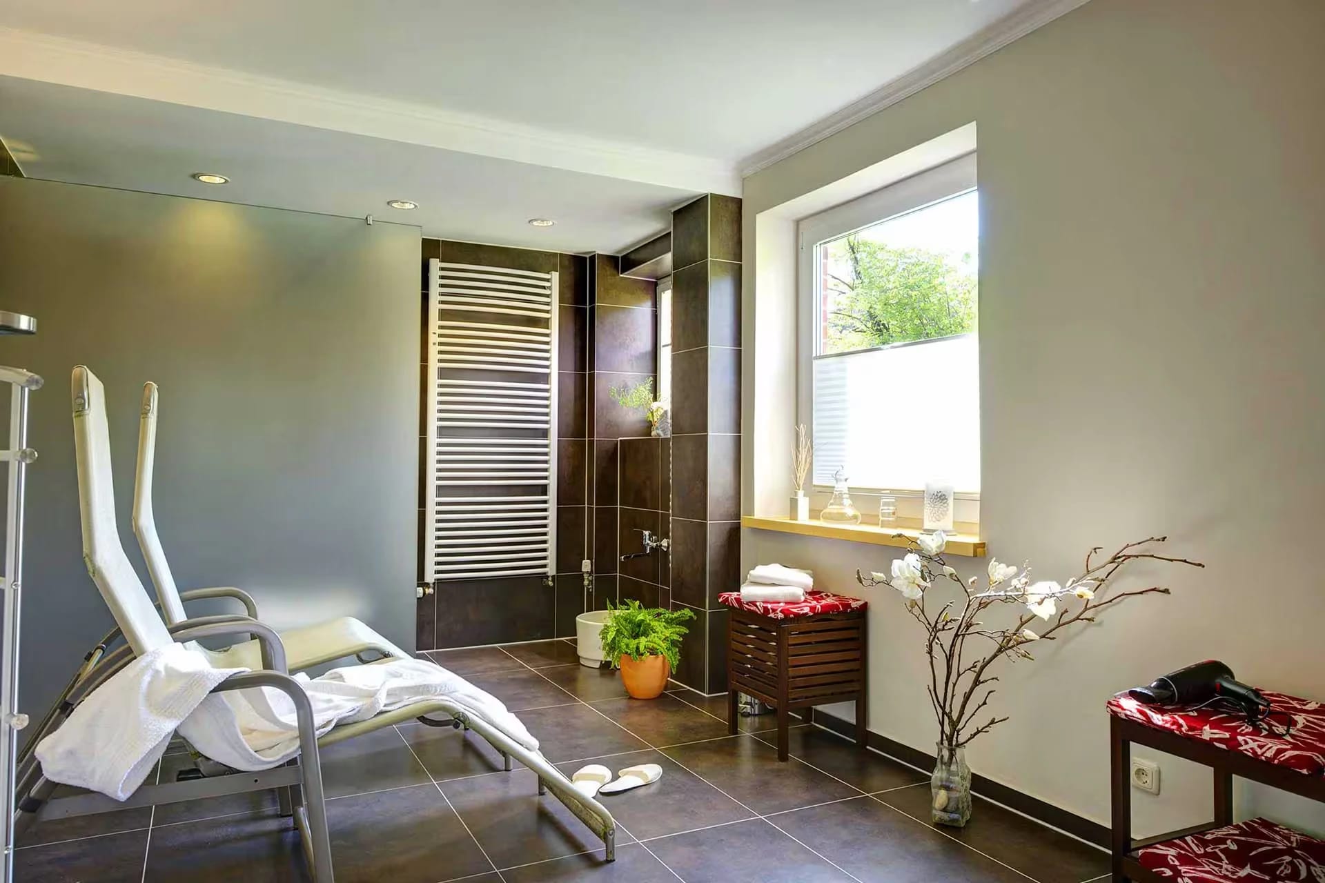 Ruheraum der Wellnessoase mit Relaxliege, Dusche und Handtüchern am Fenster