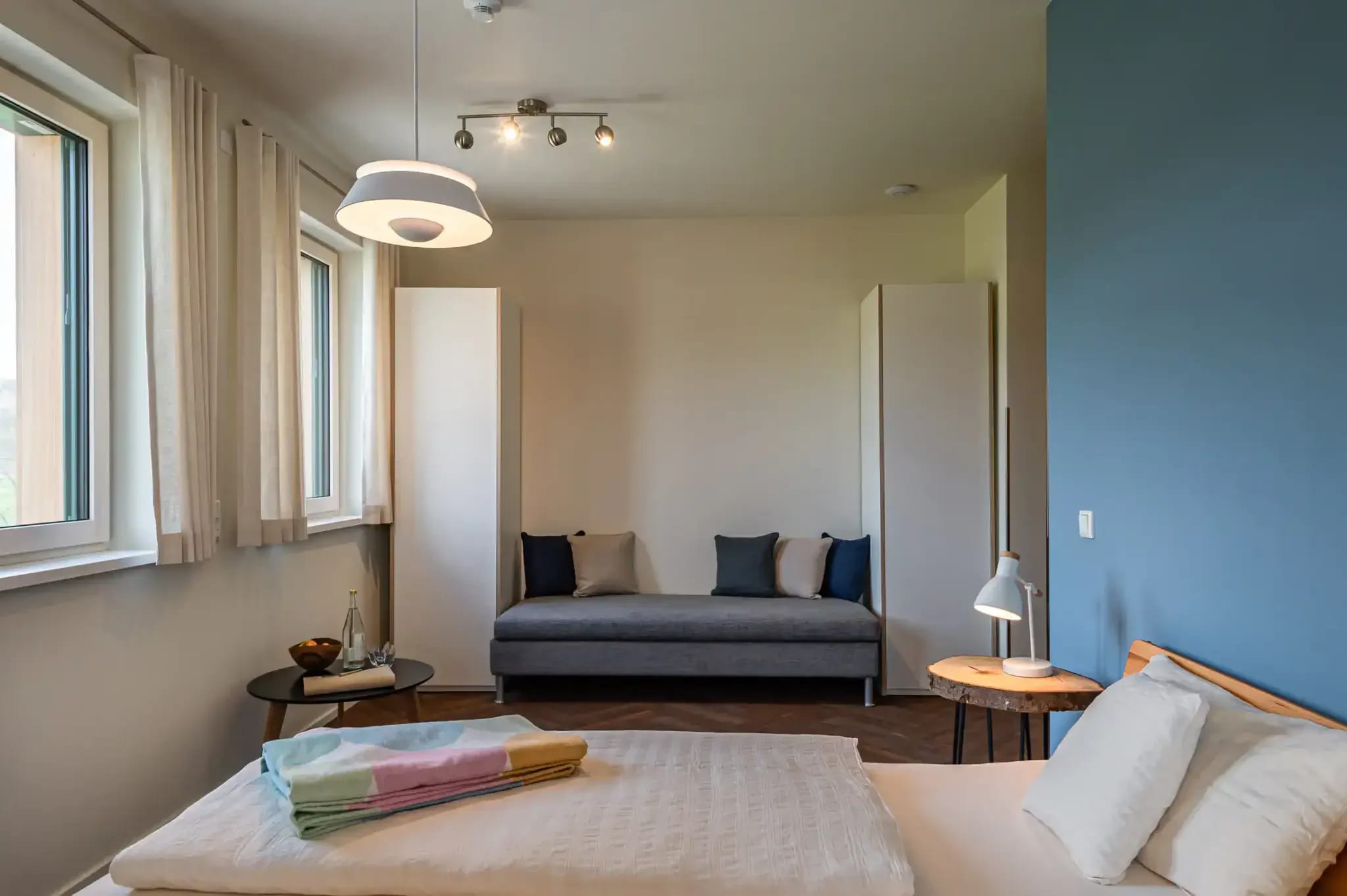 Zimmer mit blauer Wand, Doppelbett, Tagesbett und Eckfenster