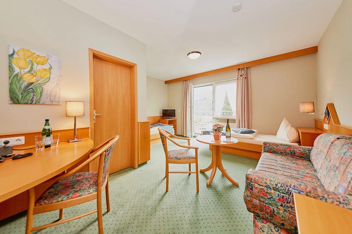 Zimmer mit Sofa, Sitzecke, Schreibtisch und Balkontür