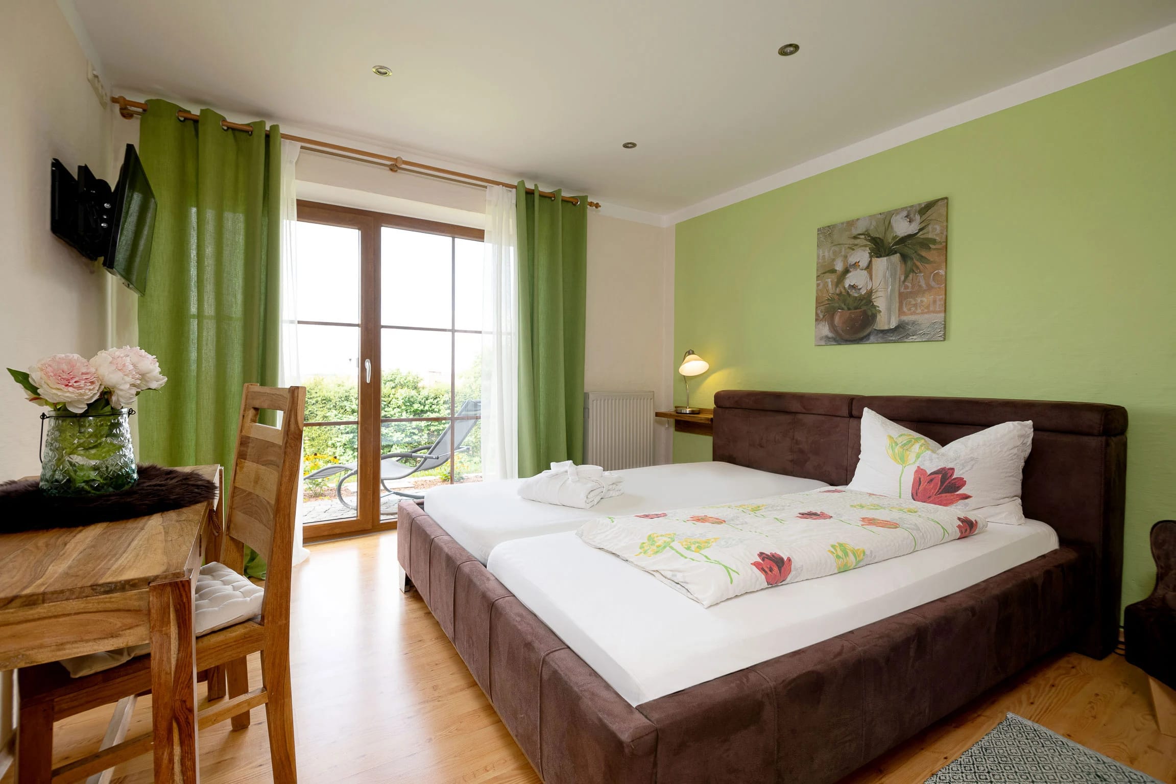 Doppelzimmer mit grüner Wand, Polsterbett, grünen Vorhängen, Balkontür und Sitzecke am Fenster