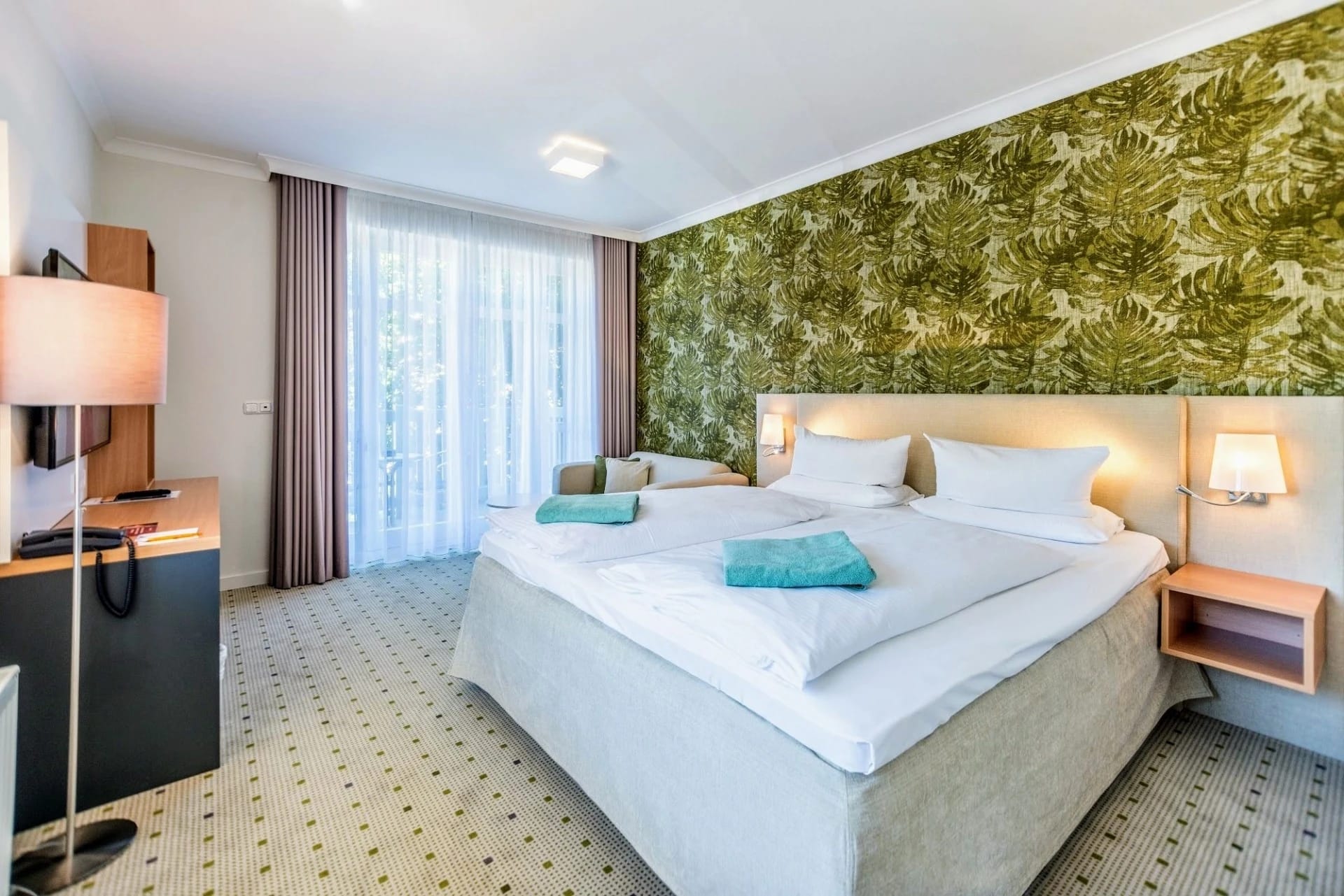 Modernes Doppelzimmer mit grüner Blättertapete hinter dem Bett