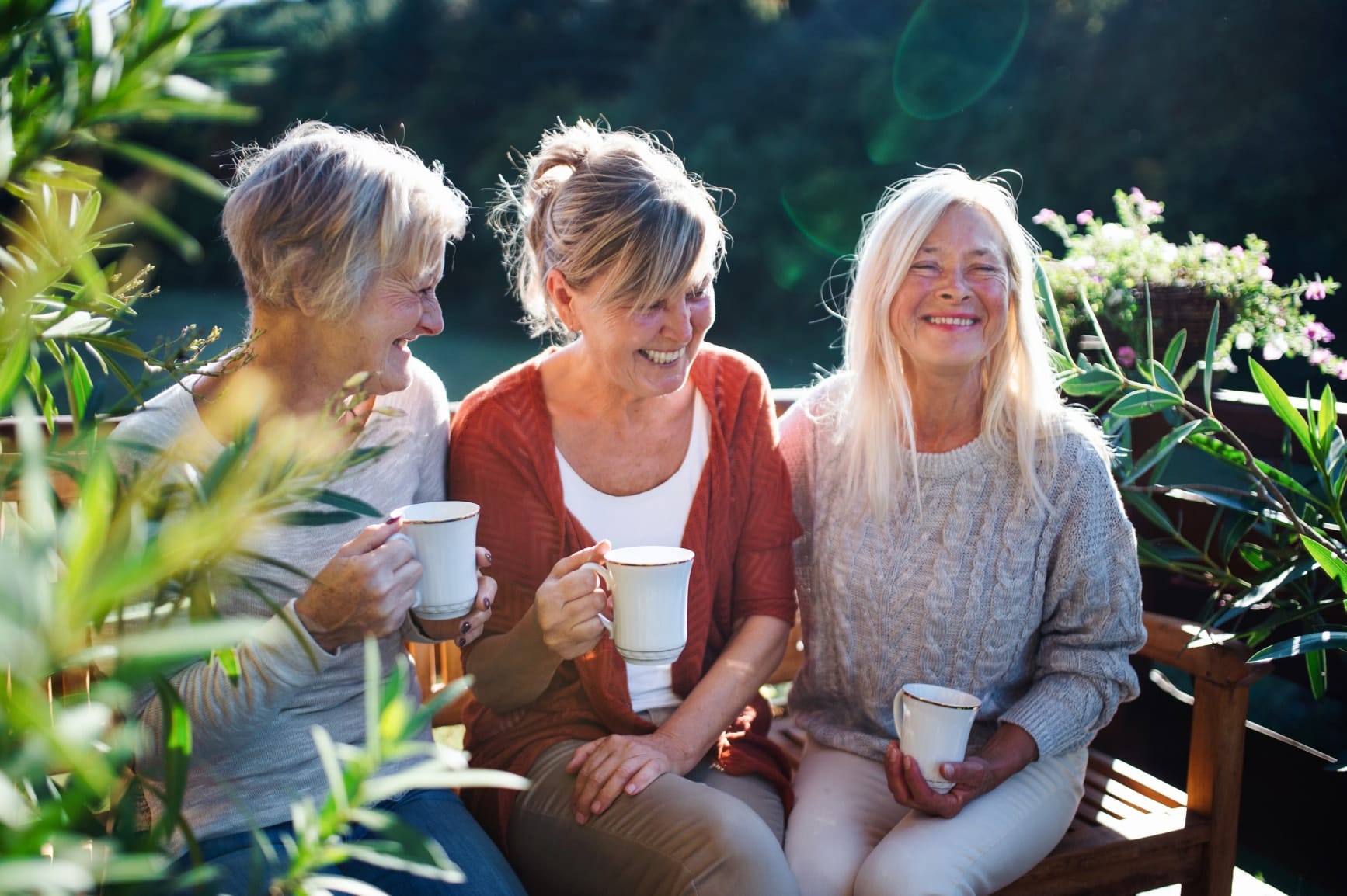 Drei Damen genießen eine Tasse Tee auf einer sonnigen Bank mitten in der Natur
